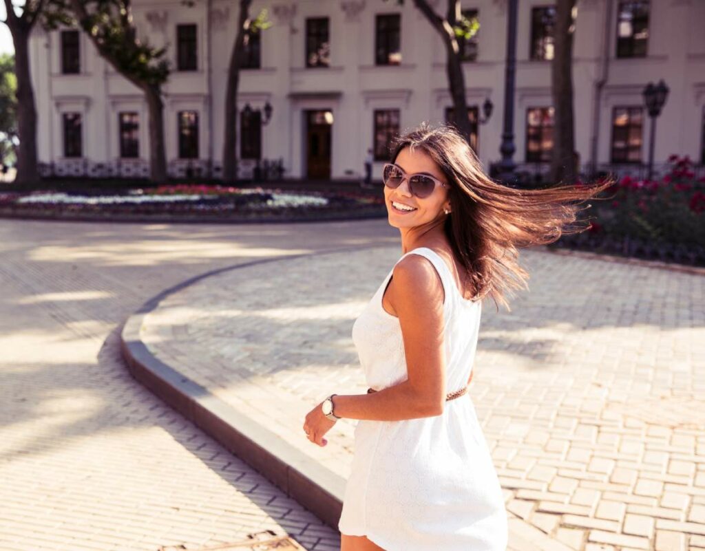 Happy young woman in sunglasses who’s just moved to a new city alone takes a walk in the fresh air